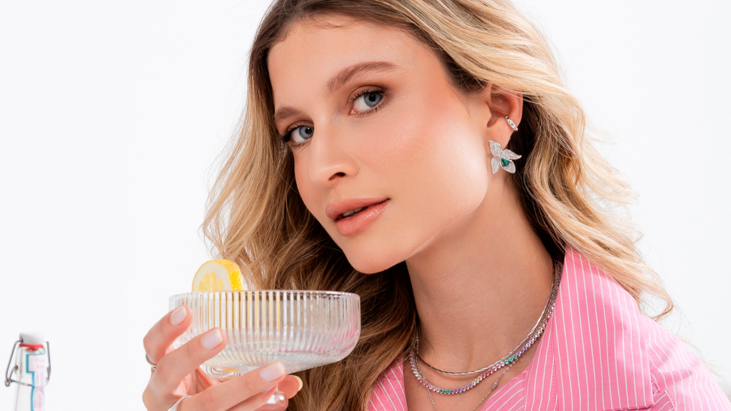 Modelo usando mix de semijoias para o Carnaval 2026, destacando brinco de orquídea e colar riviera colorida.